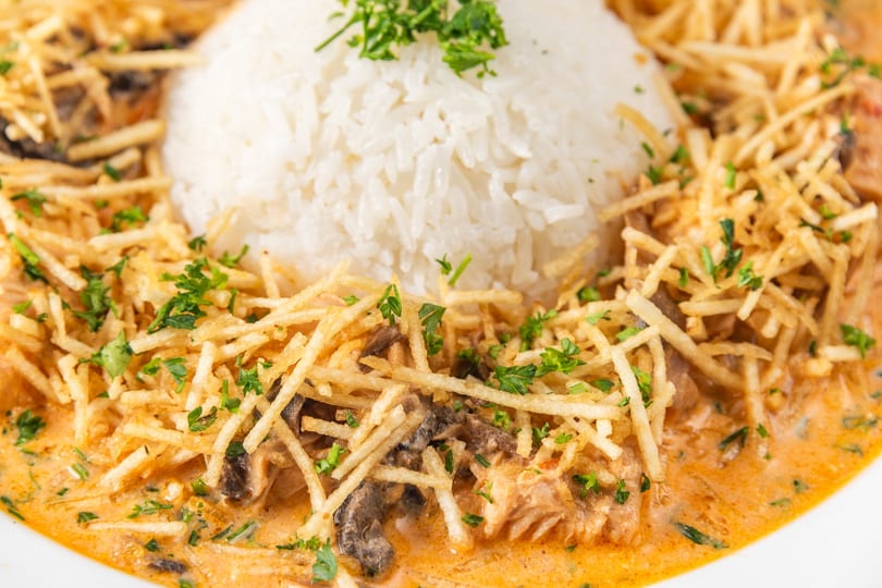 Creamy salmon and mushroom stroganoff with crispy potato sticks and a mound of white rice.