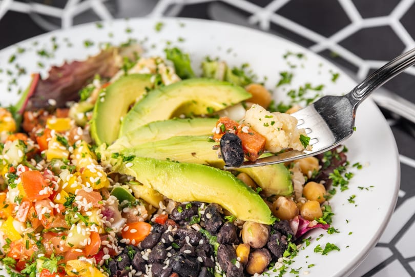 Colorful vegan salad with avocado, black beans, chickpeas, and salsa, with a fork lifting some food.