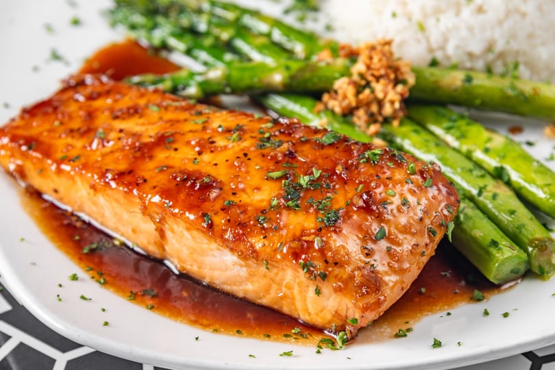 Glazed salmon with asparagus, white rice, and crispy garlic on a white plate.