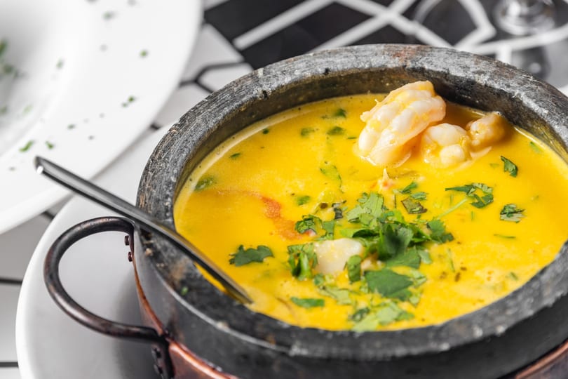 Bright yellow shrimp moqueca, garnished with fresh cilantro, served in a rustic stone pot.